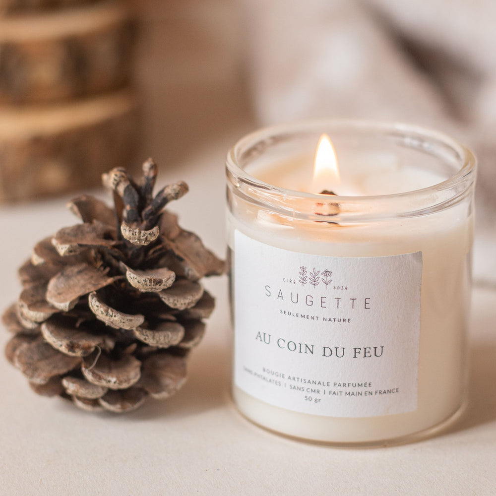 Bougie parfumée Saugette allumée près d’une pomme de pin, moment cocooning et douceur d’hiver
